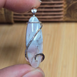 Close-up of a hand holding a silver wire-wrapped stone pendant against a wooden background