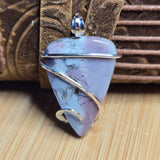 Purple stone pendant with silver wire wrapping on a textured surface
