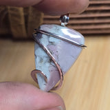 Hand holding a pink stone pendant with silver wire wrapping on a wooden surface