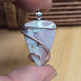 Pink stone pendant with silver wire wrapping held between fingers on a wooden surface