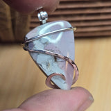 Close-up of a stone pendant with silver and rose gold wire wrapping held between fingers.