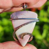 Pastel colored jasper in sterling silver held in hand on blurred green background