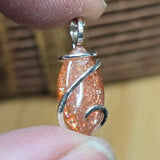 Orange glittery pendant with silver wire wrapping held between fingers against a blurred background