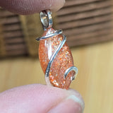 Close-up of a sparkling orange pendant with silver wire wrapping held between fingers.