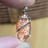 Close-up of a glittery stone pendant with silver wire wrapping held between fingers.