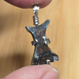 Metallic pendant held between fingers against a blurred background