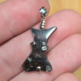 Silver and stone pendant held between fingers on a neutral background