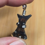 Pallasite Meteorite Pendant in silver held between fingers against a blurred background