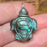 Turtle-shaped pendant with a metallic sheen held between fingers.