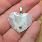 Heart-shaped pendant held in a hand with a blurred background