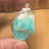 Turquoise crystal stone pendant with silver chain held between fingers against a blurred background