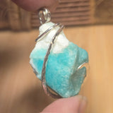 Turquoise crystal stone pendant with silver wire wrap held between fingers against a blurred background