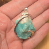 Turquoise crystal stone pendant on a silver chain held in a hand.