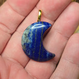 Blue stone pendant on a gold chain held in a hand