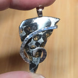 Silver pendant held between fingers against a blurred background