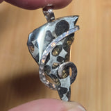 Silver pendant with black and white pattern held between fingers against a beige background