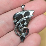 Silver pendant held between fingers with a blurred background