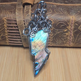 Silver lightning bolt pendant with gemstone on a wooden surface
