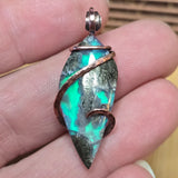 Aurora Opal pendant with copper wire wrapping held between fingers
