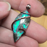 Multicolored stone pendant held between fingers with a blurred background