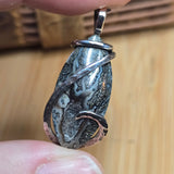 Close-up of a hand holding a silver pendant with a textured design on a wooden surface.