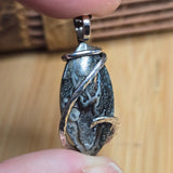 Close-up of a hand holding a silver pendant with a textured stone design on a wooden surface.