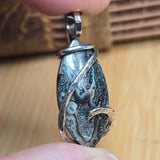 Hand holding a silver pendant with a textured design against a wooden background
