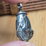 Silver pendant with a stone held between fingers on a wooden surface