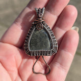 Hand holding a silver wire-wrapped pendant with a green stone
