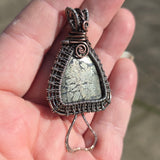 Hand holding a wire-wrapped pendant with a textured stone