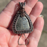 Hand holding a wire-wrapped pendant with a stone-like center