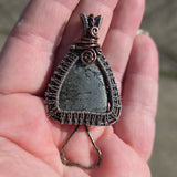 Hand holding a wire-wrapped pendant with a metallic stone