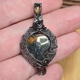 Silver and copper wire-wrapped pendant with a central stone held between fingers