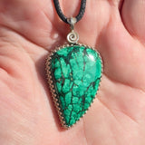 Green stone pendant on a black cord held in a hand