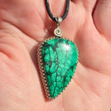 Green teardrop pendant on a black cord held in hand