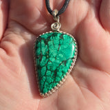 Green gemstone pendant on a black cord held in a hand.