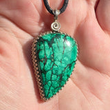 Green stone pendant on a black cord held in hand