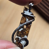 Close-up of a silver and brown pendant held between fingers on a beige background