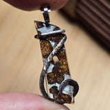 Close-up of a unique pendant held between two fingers against a neutral background