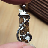 Close-up of a silver and brown pendant held between fingers with a blurred background