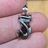 Silver pendant held between fingers with a blurred background
