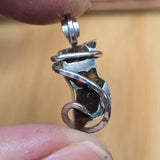 Silver Pallasite pendant held between fingers against a beige background