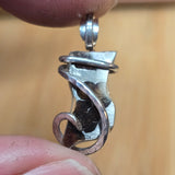 Close-up of a silver pendant held between fingers against a beige background