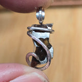 Silver pendant held between fingers against a beige background