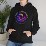 Person wearing a black hoodie with colorful design and text, standing indoors next to a plant.