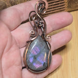 Hand holding a Labradorite pendant with intricate copper wirework