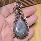 Teardrop-shaped pendant with copper wire wrapping held in a hand on a wooden surface