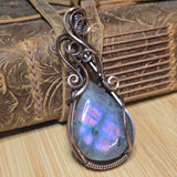 Copper pendant with a teardrop-shaped gemstone on a textured wooden surface