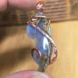Pendant with blue stone and copper wire wrapping held between fingers against a blurred background