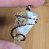 Hand holding a crystal pendant with copper wire wrapping on a wooden surface